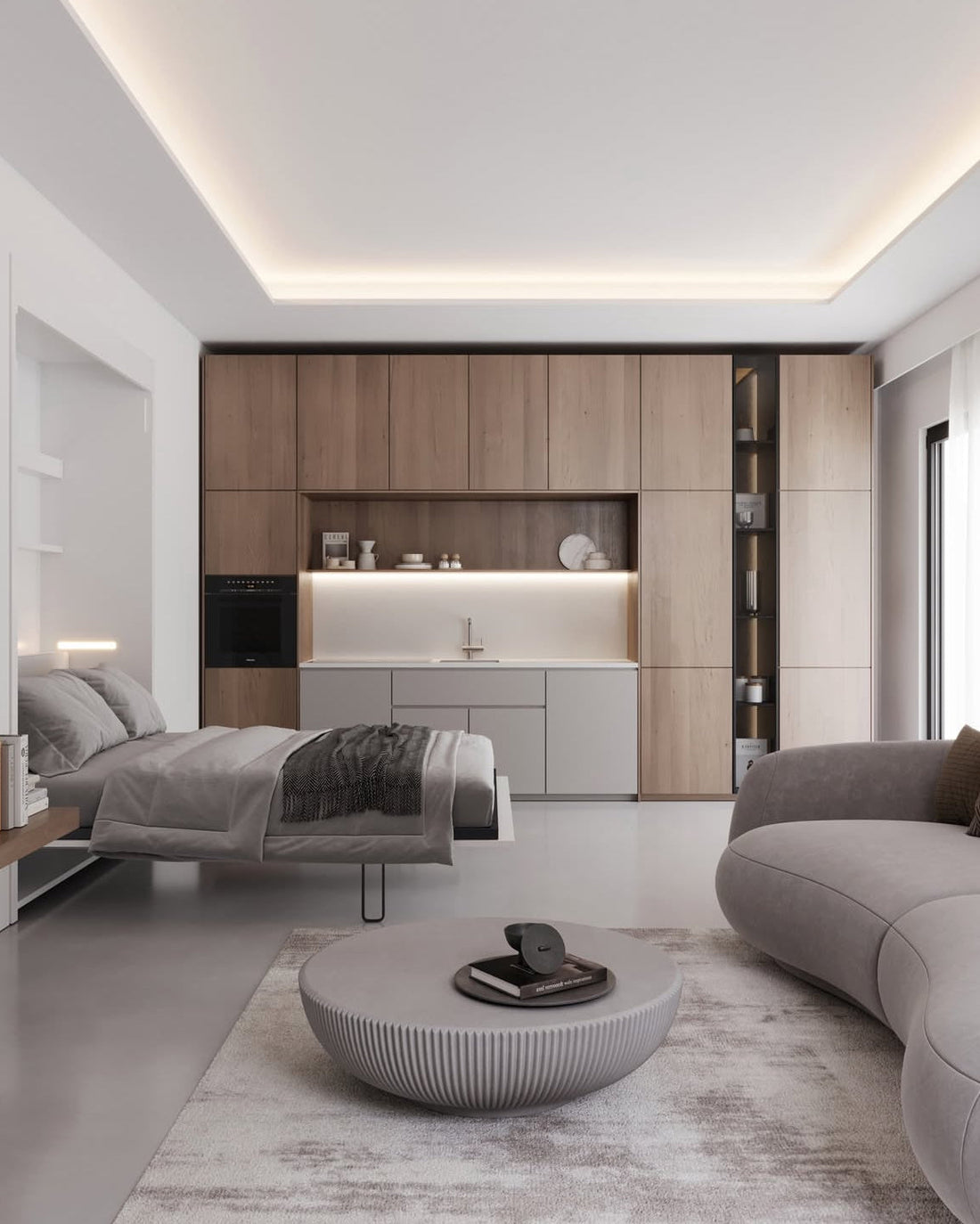 Monolocale moderno con letto a scomparsa, parete attrezzata in legno con cucina integrata, divano grigio curvo e tavolino rotondo grigio su tappeto chiaro.