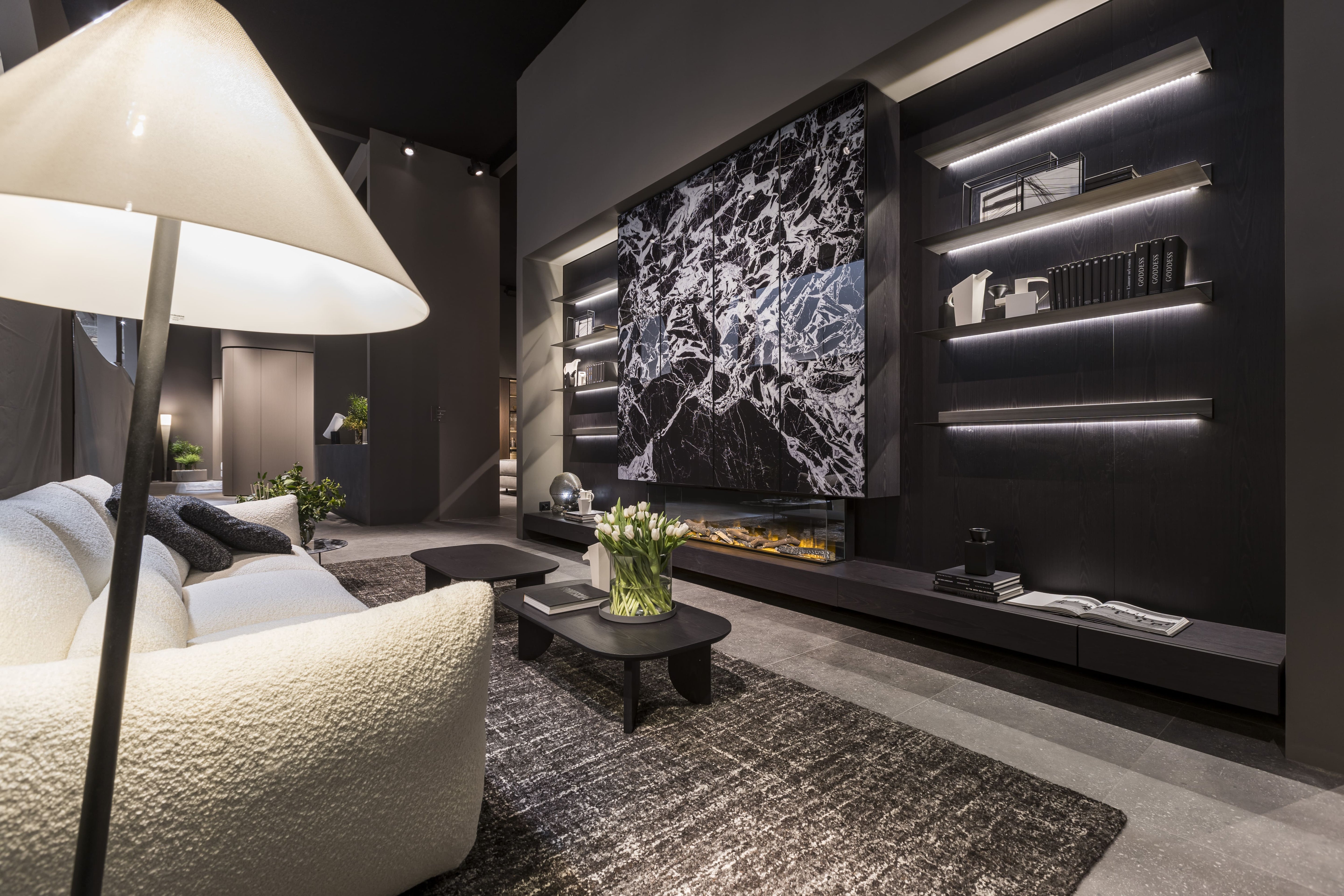 Soggiorno moderno di design con parete attrezzata nera, pannello in marmo a contrasto, mensole illuminate a LED, divano chiaro e tavolino con vaso di tulipani.