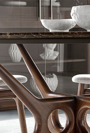 Dettaglio della base di un tavolo in legno massello con struttura scultorea e finitura naturale, in un ambiente di design.