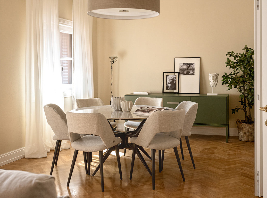 Zona pranzo moderna con tavolo rotondo in vetro, sei sedie chiare, pavimento in parquet e arredi minimal in un ambiente luminoso.